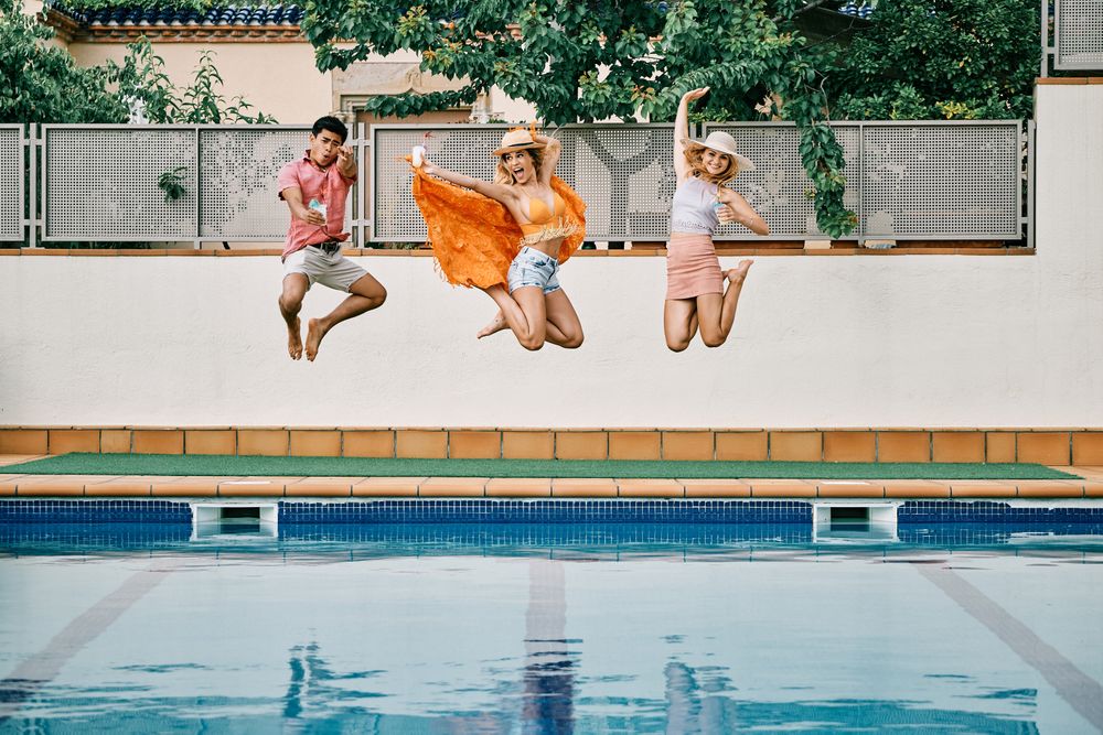 two young women and a man jumping by the pool