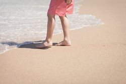 Crop legs near sea water on sand