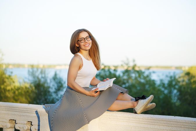 Happy woman perched atop a wall with book