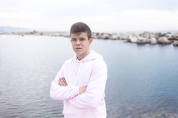 Serious male teenager with crossing arms standing on promenade while looking at camera