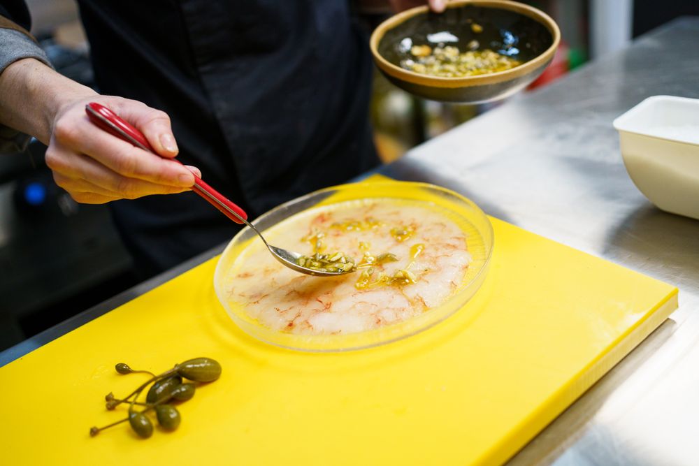 Hands placing sauce on delicate prawn appetizer