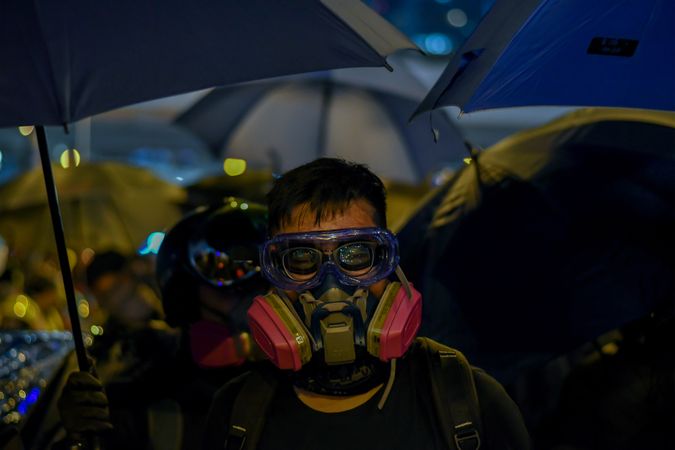 Man wearing gas mask standing under an umbrella during Hong Kong protests