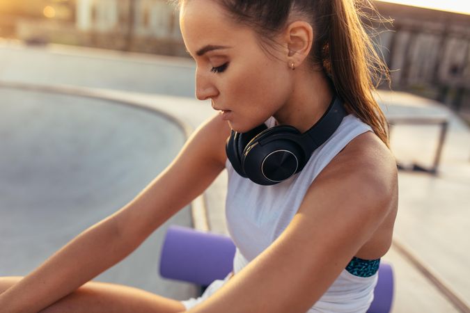 Fitness female sitting with headphones around her neck after exercising