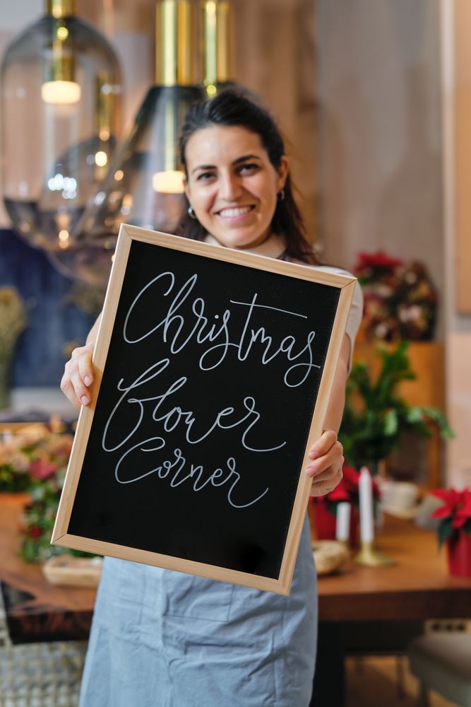 Cheerful female owner demonstrating chalkboard in flower shop