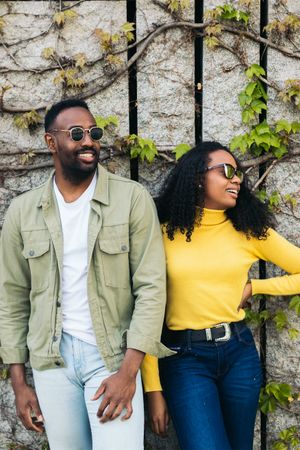 Black couple posing in front of wall with foliage