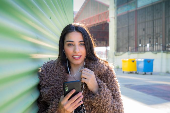 Trendy woman with smartphone near wall