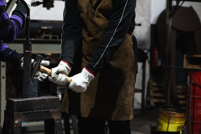 Professional blacksmith making form of metal detail with hammer