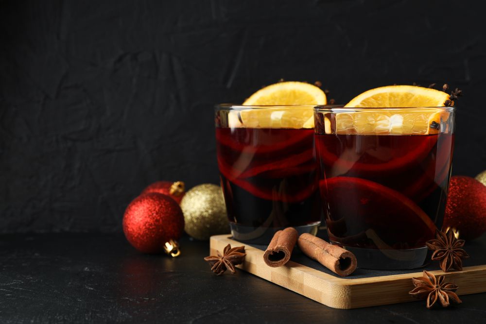 Glasses of tasty mulled wine and christmas baubles on dark background, space for text