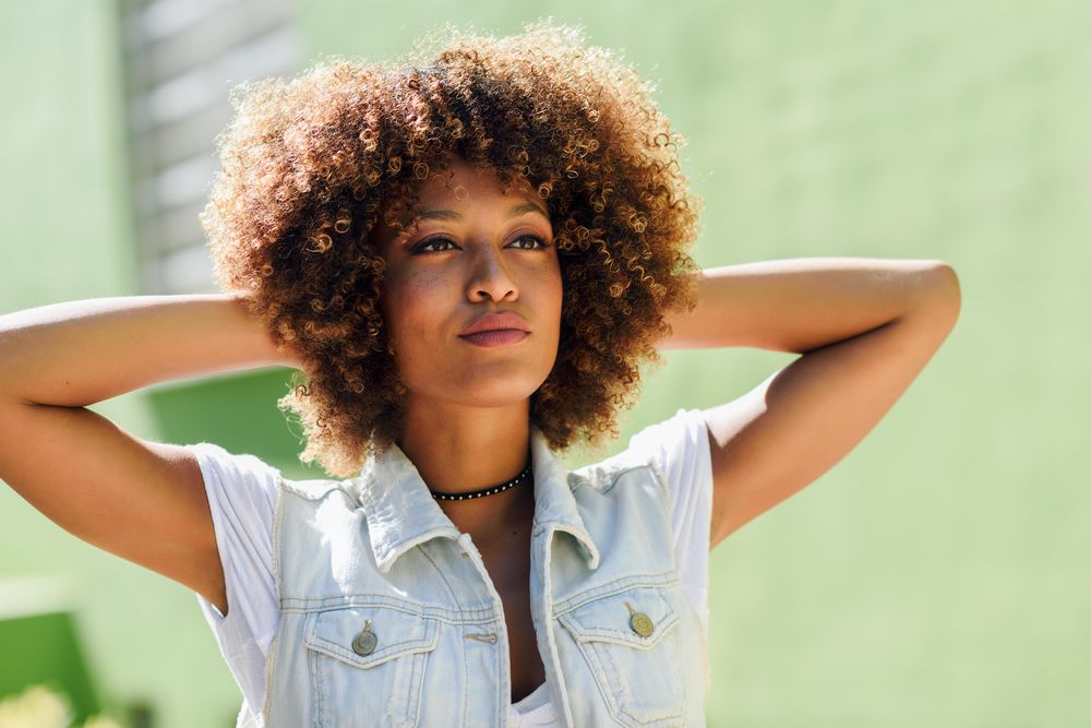 Woman wearing jean vest with arms up in front of green wall