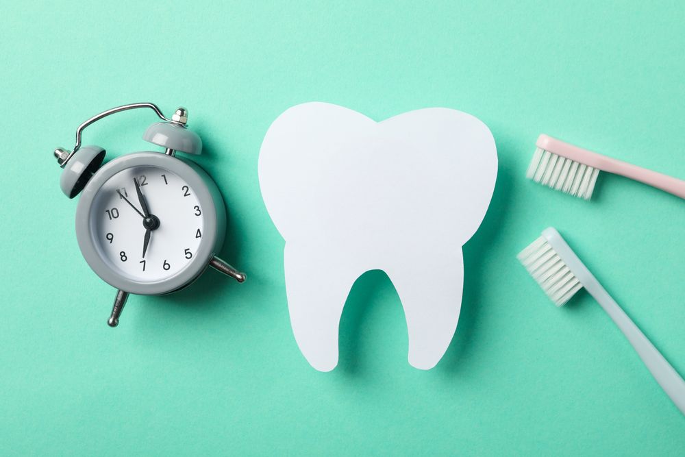 Clock, tooth and toothbrushes on mint background, top view