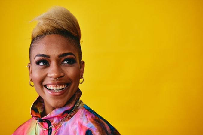 Studio shot of trendy Black woman in bold 80s windbreaker jacket and gold jewelry