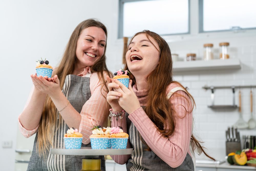 Daughter laughing with mother at home with cupcakes