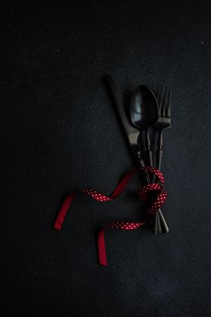 Dark cutlery on dark background tied with dotted red ribbon