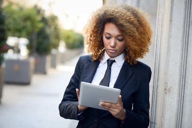 Serious female in suit standing outside checking her tablet