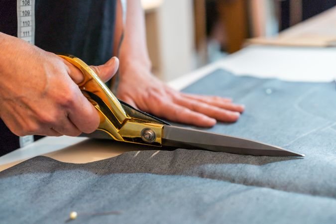 Close-up of fashion designer hands using scissors to cut textile at work table