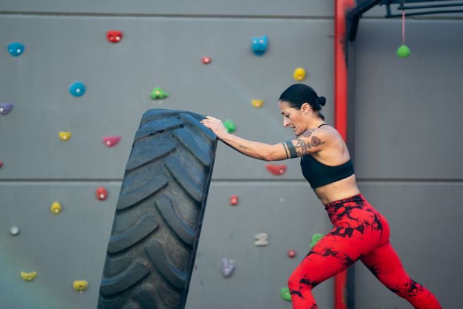 Side view of fit woman flipping a truck wheel in a gym