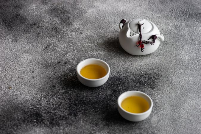 Two green tea cups and tea pot on grey counter