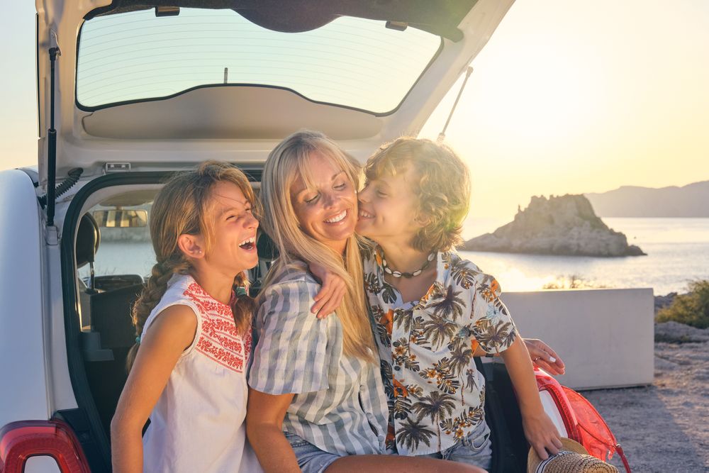 Happy mother and children sitting together on car trunk
