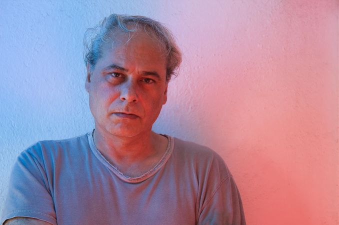 Portrait of disappointed middle aged man in gray shirt against light background in UV lit studio