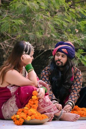 Indian man sitting beside woman in pink sari on ground beside trees