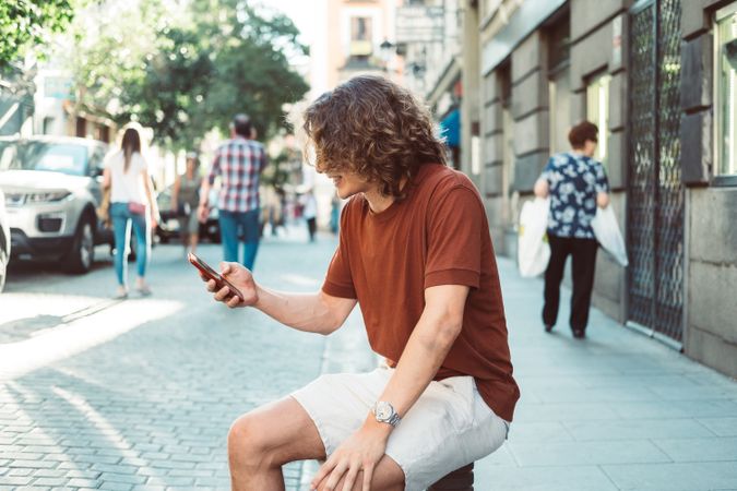 Amused man with longboard talking on phone while resting on street