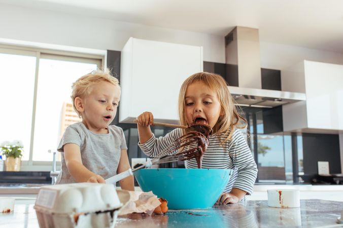 Kids preparing cake batter with girl licking batter from spatula