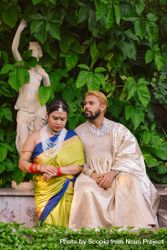 Indian man and woman sitting beside statue in a garden 49YOW4