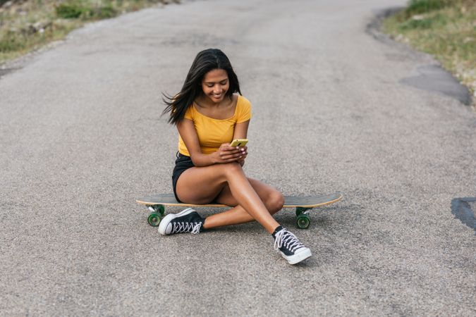 Cheerful woman using mobile phone while sitting on longboard