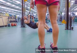 Legs of female trainer looking on at person using calisthenics in gym 5l1ZV4