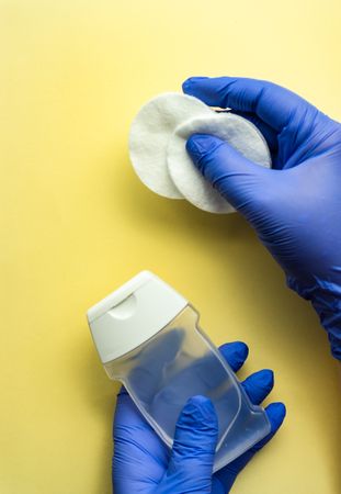 Top view of yellow table with hands wearing protective blue gloves holding soap with cotton swabs