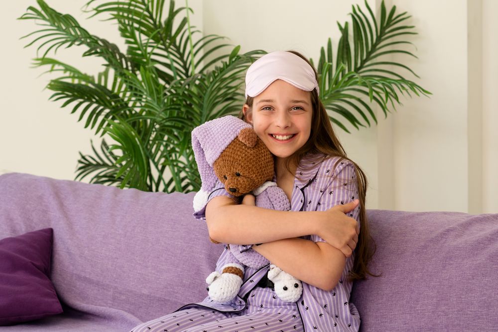 Girl hugging teddy bear, smiling while seated on couch.