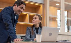 Woman sitting at laptop speaking to male colleague
