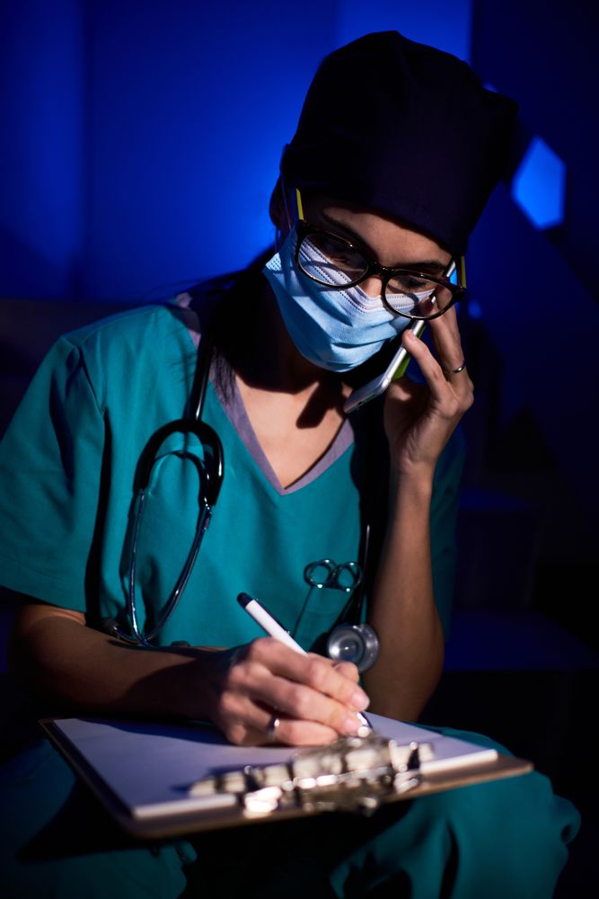 Female doctor writing medical report while talking on cellphone