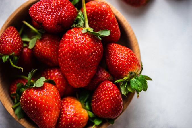 Close up of strawberries in wooden bowl full on grey counter with copy space
