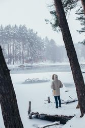 Man in parka outside looking out onto lake in snowy forest