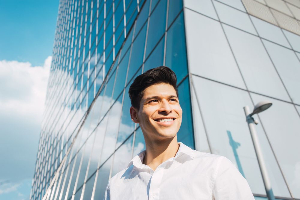 Smiling young man in sunlight under skyscraper