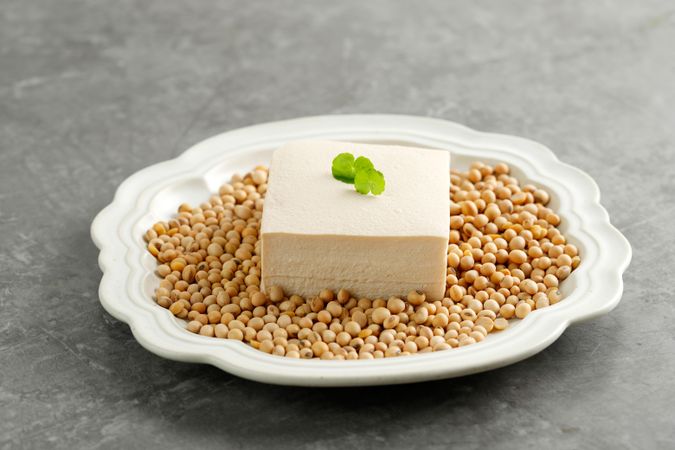 Tofu block served with garnish atop soybeans on plate