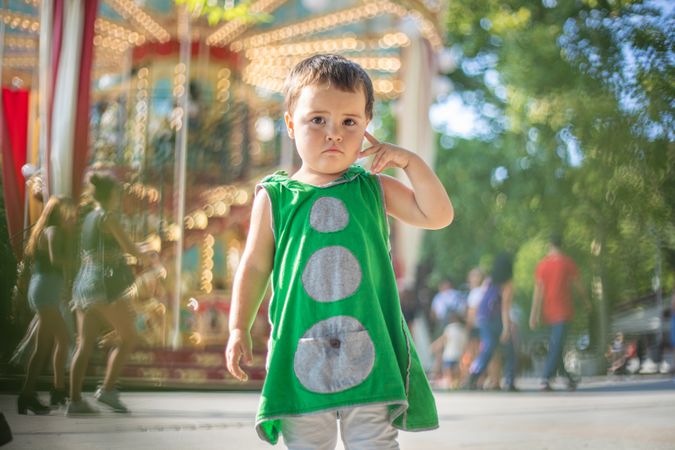 Child standing near moving carousel and dreaming at fair