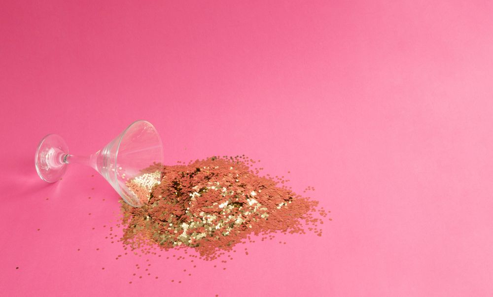 Spilled martini glass full of gold glitter on pink background