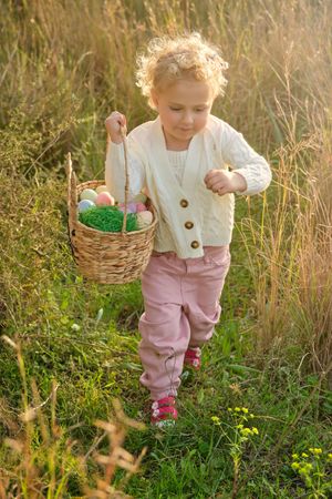 Cute girl carrying basket with Easter eggs in countryside