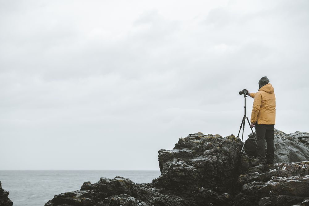 Man standing on rock and taking picture of sea