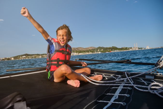 Excited boy in boat floating on sea water