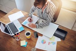Top view of woman taking notes from laptop in home office with coffee