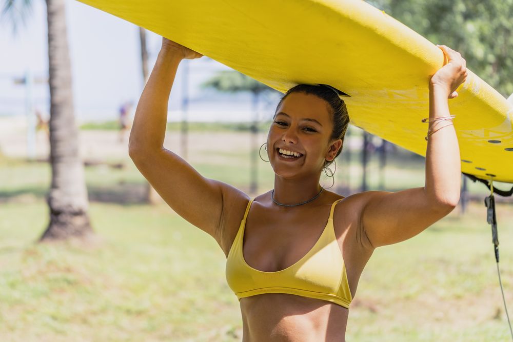Woman in bikini with bright paddleboard on beach