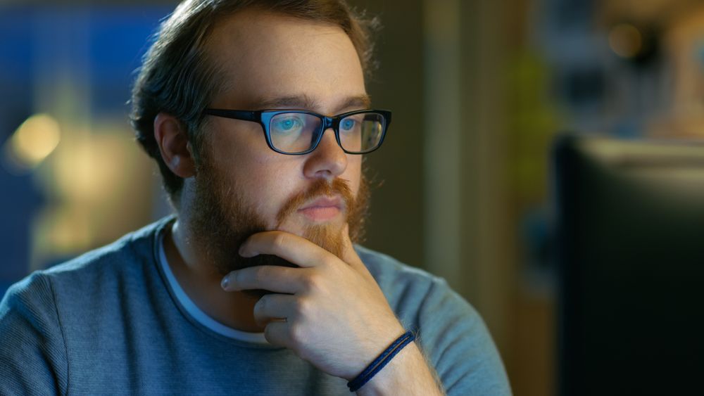 Young Bearded Creative Man Thinks on a Problem While Working on His Personal Computer.
