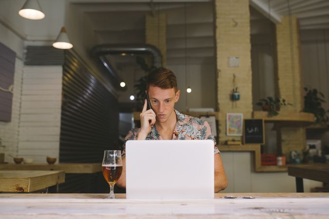 Man talking on smartphone while browsing laptop