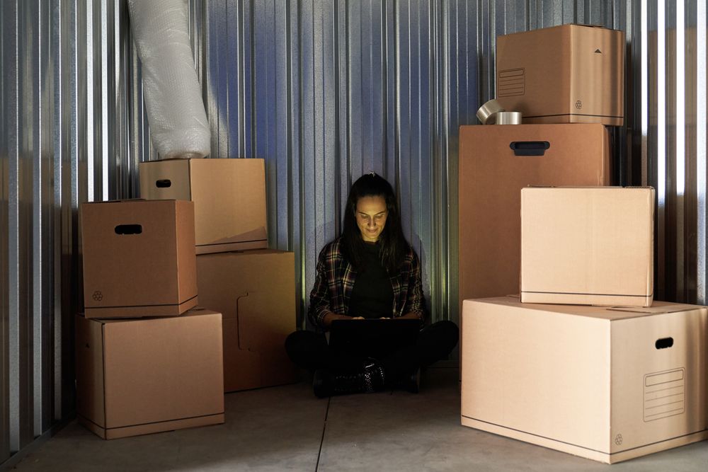 Young pretty woman inside a warehouse to store moving boxes organizing with her laptop