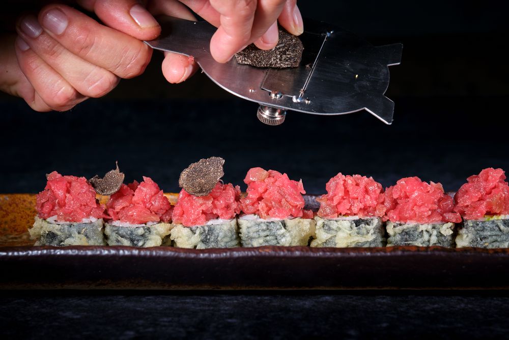 Faceless chef slicing truffle on sushi rolls with tuna
