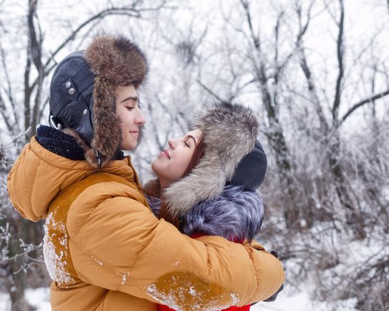 Cute teenage couple holding each other and gazing into each others eyes in wintery forest