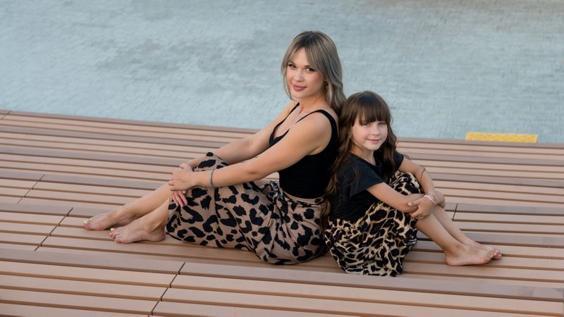 Long-haired mother and daughter sitting on bench back to back